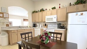 A compact kitchen with wooden cabinets, a white refrigerator, a microwave, a stove, and a sink. There is a dining table with chairs and a vase of flowers. - Modest Charmer W/ Private Pool (Clermont)
