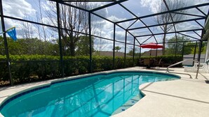 A swimming pool with a clear blue water, surrounded by a covered area with chairs and an umbrella. - Modest Charmer W/ Private Pool (Clermont)