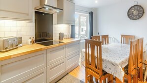 Una cocina moderna con armarios blancos, horno integrado y un comedor con sillas y mesa de madera.