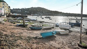 Zona costera con barcos en la orilla y una vista de un pueblo al fondo.