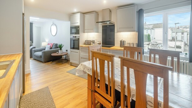 Una cocina moderna con electrodomésticos integrados, un comedor con sillas de madera y vistas a la ciudad a través de grandes ventanales.