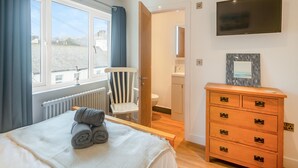Un dormitorio con cama, una silla, cómoda, televisor y vistas al exterior.