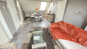 A compact living space with a sofa, a glass coffee table, a dining table with chairs, and a kitchen area with a sink and cabinets. - A 10km de Bxl ,2ch, Pour 7 ,parck,meublé,bus,train (Asse)