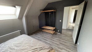 A bedroom with a sloped ceiling, a bed with a patterned bedspread, a wooden shelf unit, and a wardrobe. - A 10km de Bxl ,2ch, Pour 7 ,parck,meublé,bus,train (Asse)