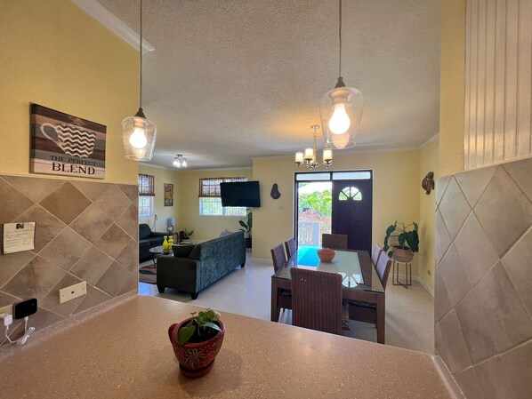 A modern kitchen with a dining area, a living room, and a large window.