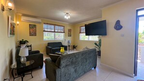 A living room with a sofa, a coffee table, a flat-screen TV, and a window with blinds.