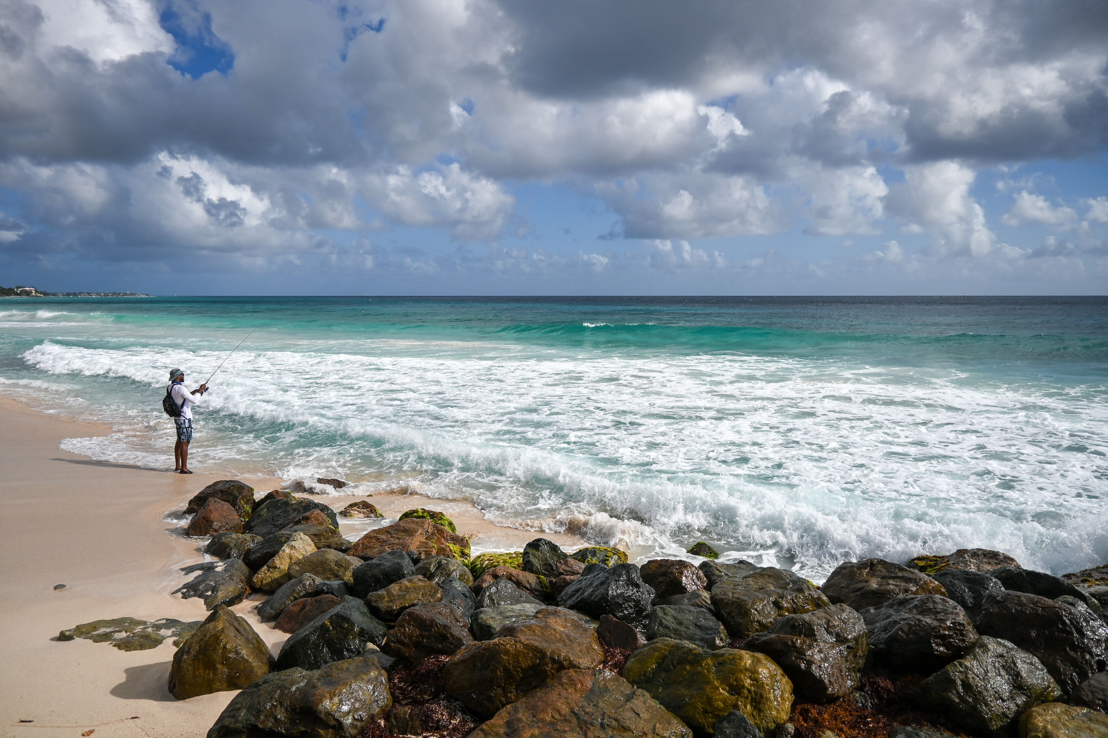 A beach with large rocks and a person fishing.