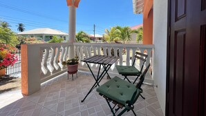 A covered outdoor area with a tiled floor, a white railing, and two green cushioned chairs.