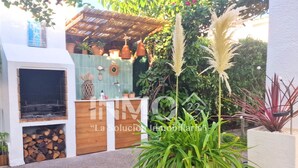 A patio area with a barbecue grill, potted plants, and a tiled wall.