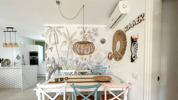 A dining area with a white table, three chairs, a woven hanging light, and a wall mural.