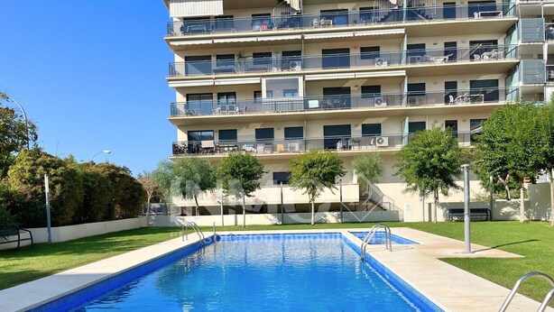 A swimming pool with a clear blue water surface, surrounded by a well-maintained lawn and trees. - Apartament in Edif. Alba de Cambrils (Cambrils)