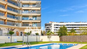 Une piscine à l’eau d’un bleu cristallin, entourée d’une pelouse bien entretenue et, en arrière-plan, d’un immeuble à plusieurs étages doté de balcons.