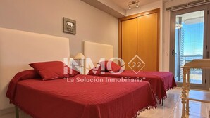 A hotel room with two beds, a wooden door, a window, and a small table. - Apartament in Edif. Alba de Cambrils (Cambrils)