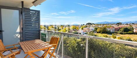 Varanda com mesa e cadeiras, vista para área residencial com casas e vegetação.