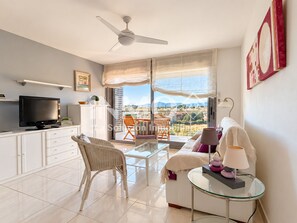 A modern living room with a flat-screen TV, a sofa, a glass coffee table, and a balcony with a view. - Apartament in Edif. Alba de Cambrils (Cambrils)