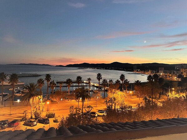 A coastal cityscape at dusk with a marina, palm trees, and a crescent moon.