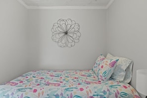 A bedroom with a bed, a colorful bedspread, a wall with a mandala design, and a white ceiling. - Contemporary Saltbox In New Seabury! (Mashpee)
