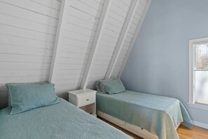 A bedroom with two single beds, a small bedside table, and a window.