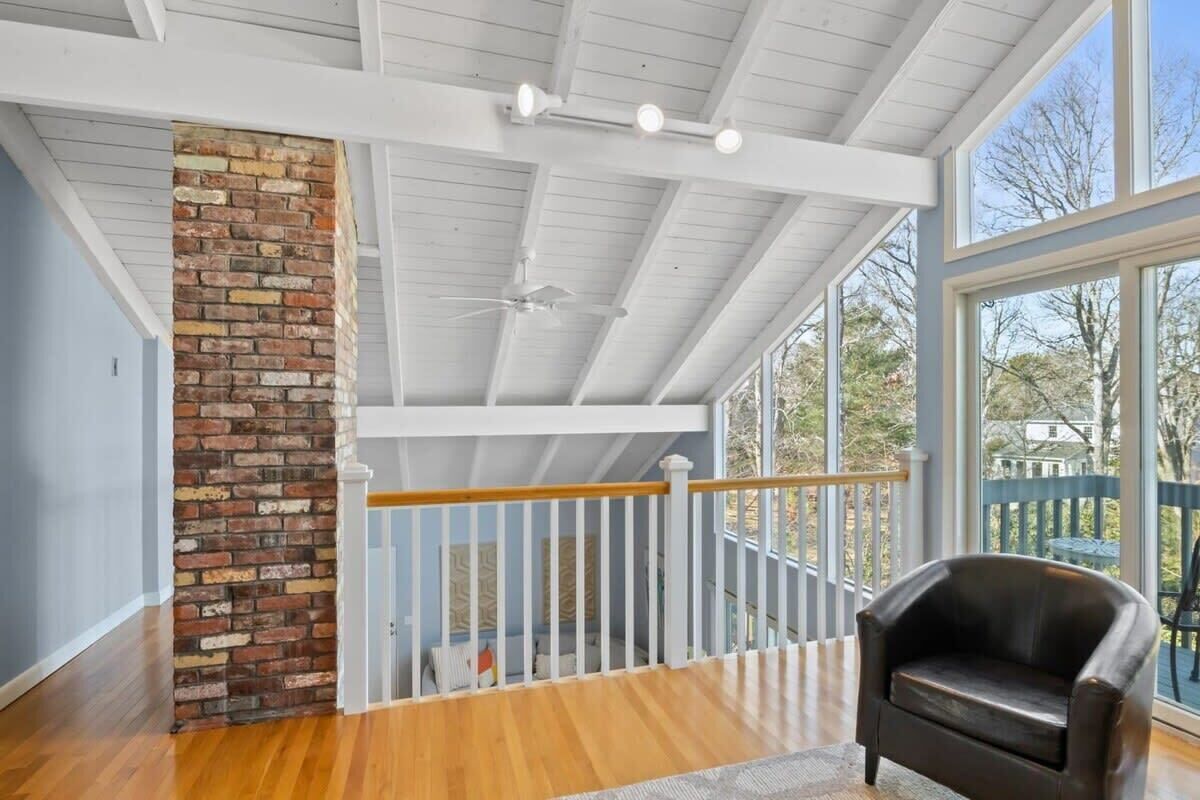 A room with a wooden floor, a brick accent wall, a white railing, and a black leather chair.