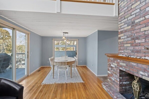 A dining area with a round table and chairs, a fireplace, and a view through large windows.