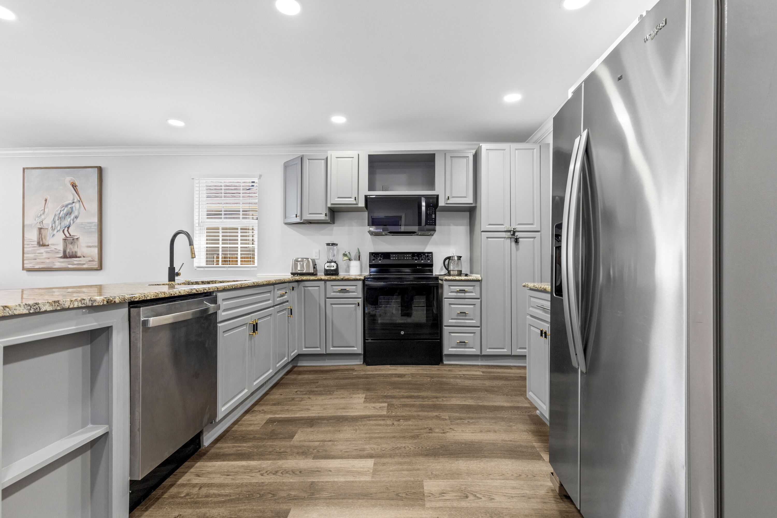 Una cocina moderna con gabinetes grises, electrodomésticos de acero inoxidable y piso de madera.