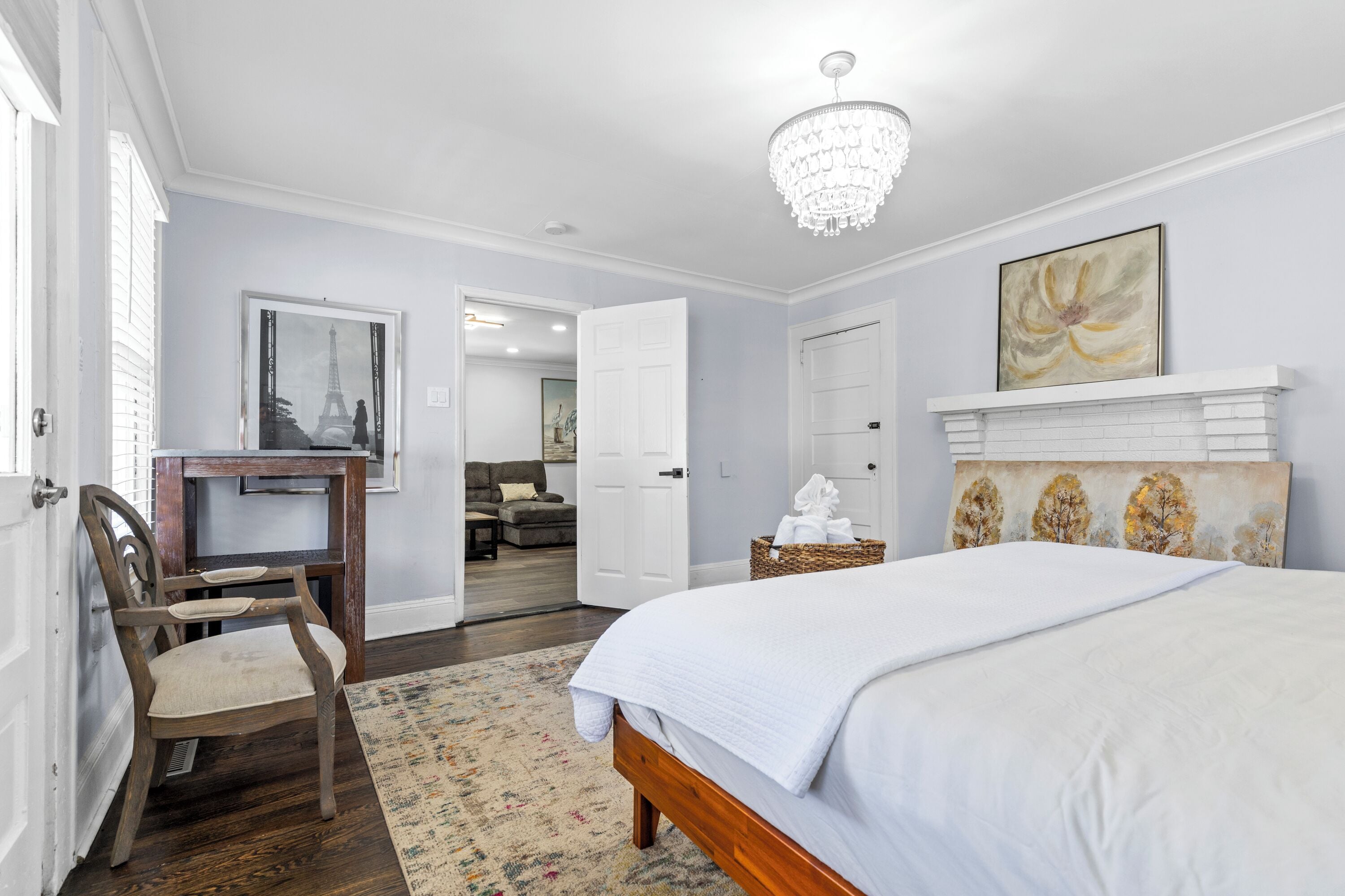 A bedroom with a large bed, a wooden chair, a desk, and a chandelier.