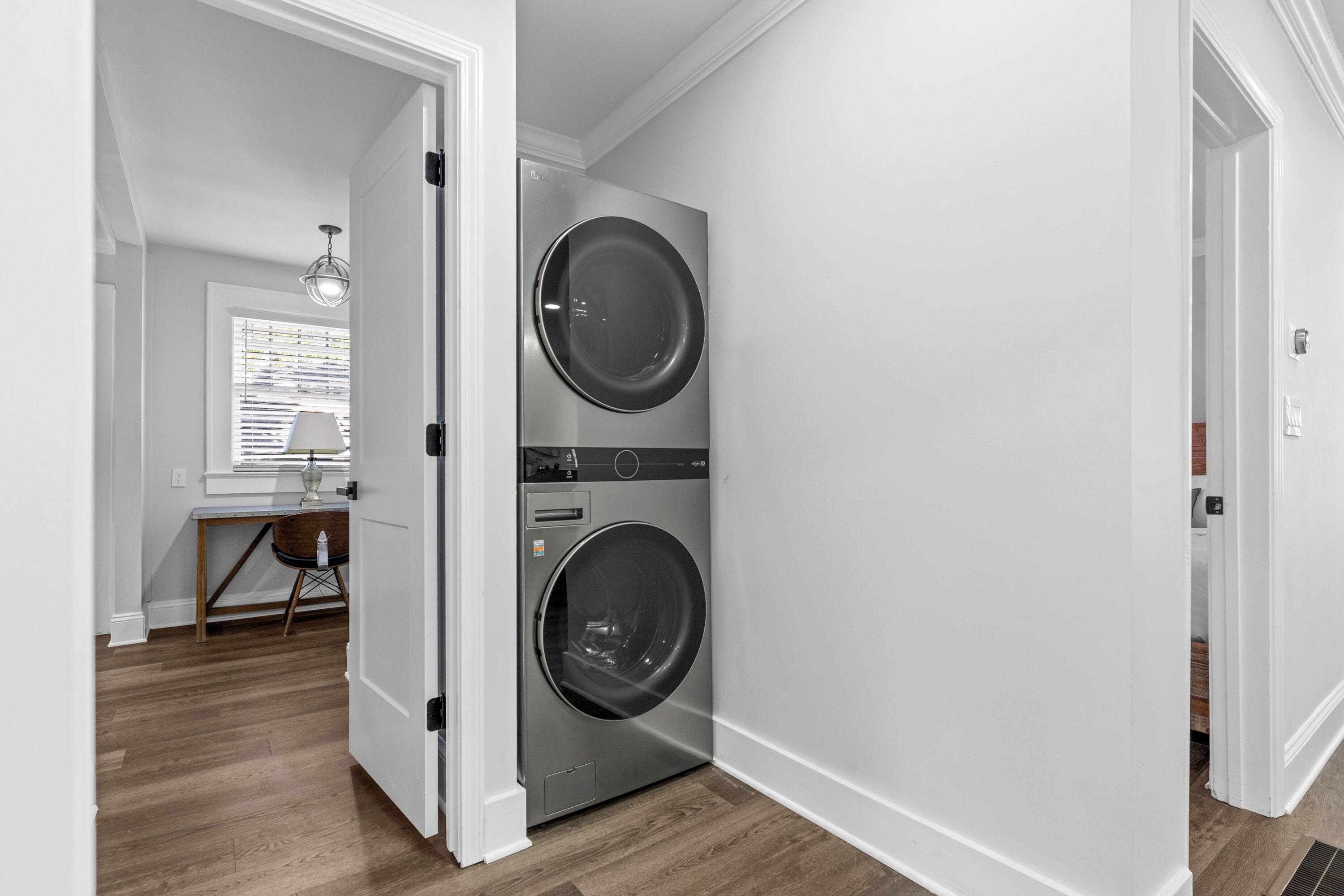 A laundry room with two stacked front-loading washing machines, a wooden floor, and a window with blinds.