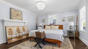 Un dormitorio con cama de madera, ropa de cama blanca, una araña, obras de arte en las paredes y una chimenea.