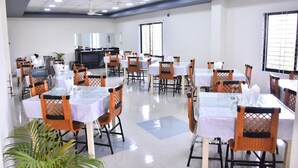Un grand espace dédié à la salle à manger, avec plusieurs tables et chaises, un téléviseur et une grande fenêtre qui laisse entrer la lumière naturelle.