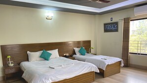 Une chambre d’hôtel avec deux lits, des têtes de lit en bois, du linge de lit blanc, une table de chevet avec une lampe et une fenêtre avec des rideaux.