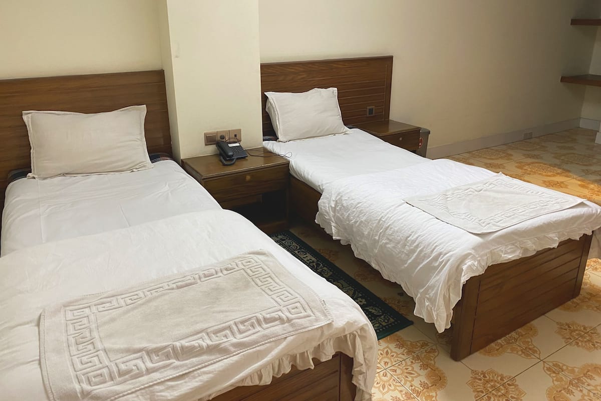 A hotel room with two single beds, wooden headboards, white bedding, a bedside table with a phone, and a patterned rug.
