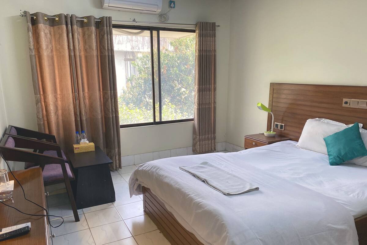 A hotel room with a bed, desk, chair, and a window with curtains.