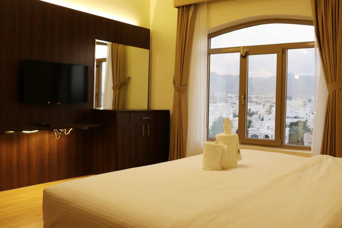 A hotel room with a bed, a flat-screen TV mounted on the wall, and a window with a view of a cityscape.