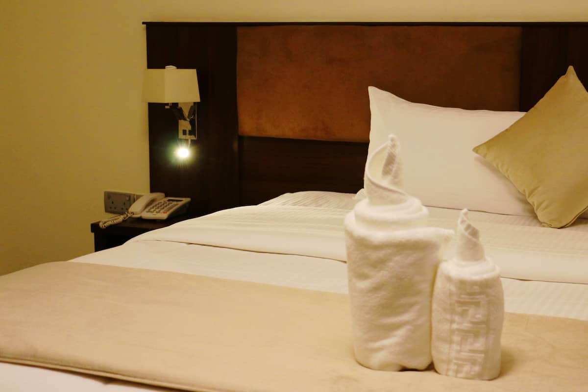 A hotel room with a neatly made bed, a bedside lamp, a phone, and a nightstand.