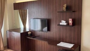 Ein modernes Zimmer mit einem dunklen Holzschreibtisch, einem flachbildfernseher an der Wand, einer kleinen Ablage mit Dekoration und einem Mülleimer.