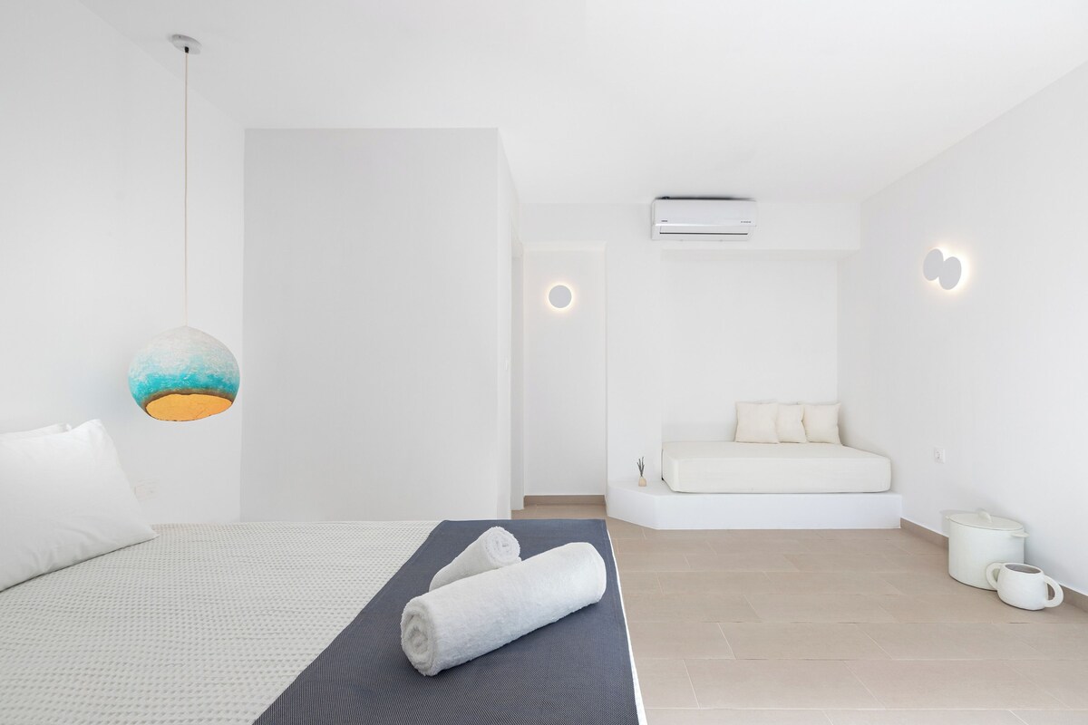 Een moderne hotelkamer met een bed, een yogamat, een handdoek, een bank en een klein tafeltje met een karaf.