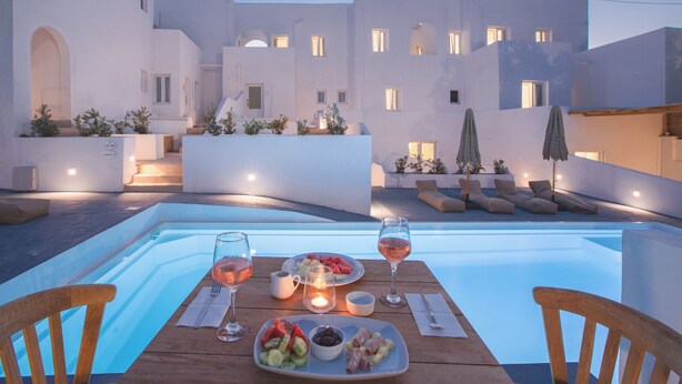 A dining area with a pool, white buildings, and outdoor seating. - VOCA HOTEL & SUITES (Santorini)