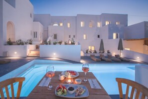 A dining area with a pool, white buildings, and outdoor seating. - VOCA HOTEL & SUITES (Santorini)