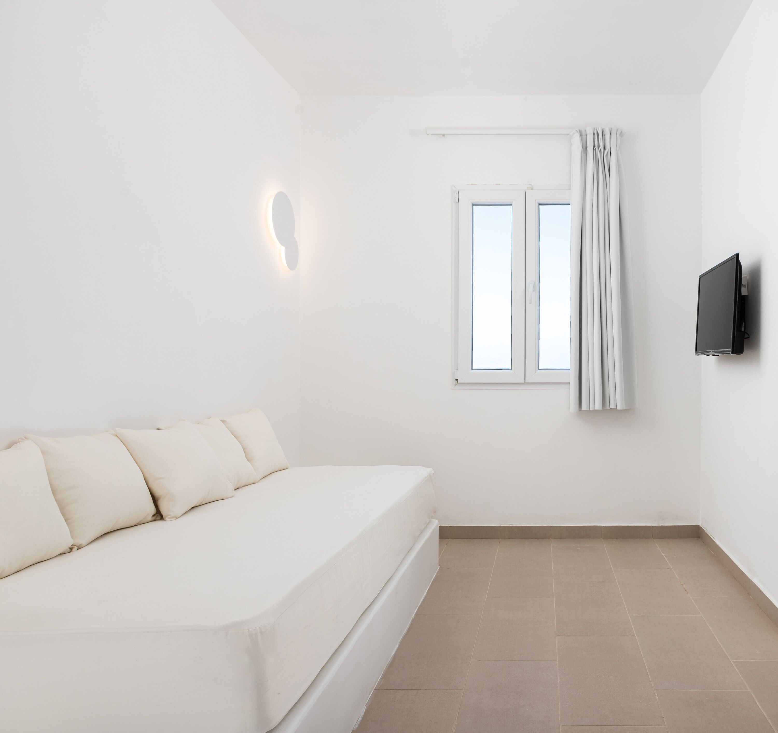 Un dormitorio minimalista con cama, televisor montado en la pared y ventana con cortinas.