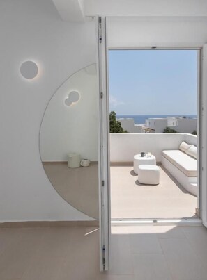 Un interior moderno con un puerta corredera que da a un balcón exterior con un sofá blanco y una pequeña mesa.