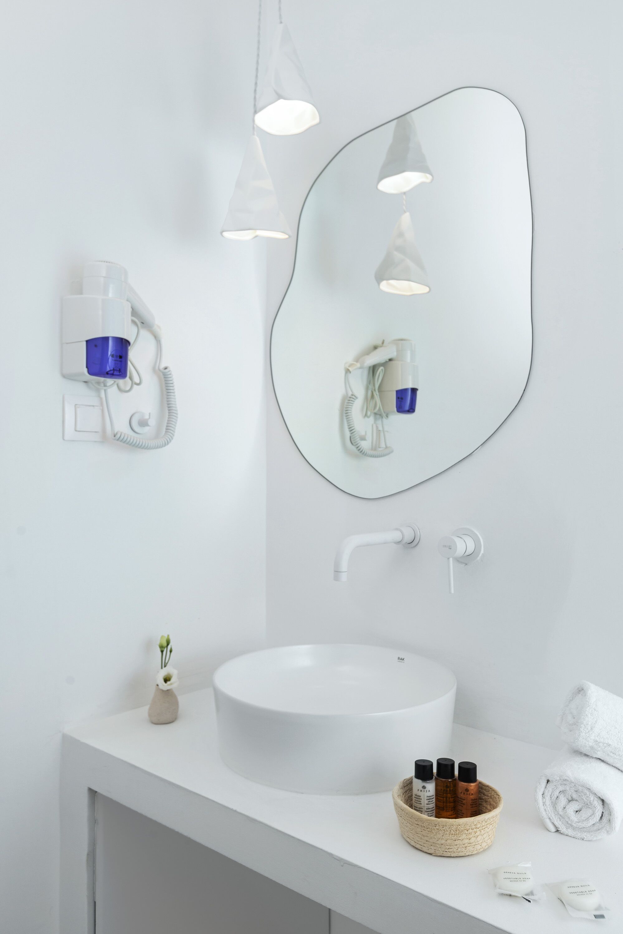 A modern bathroom with a round sink, a mirror, a hairdryer, and a towel rack.