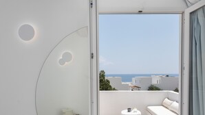 A modern interior with a large mirror reflecting a balcony area. The room has a minimalist design with a white color scheme and a large window. - VOCA HOTEL & SUITES (Santorini)