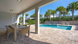 An outdoor pool area with a covered patio, lounge chairs, and a dining table with chairs. - 10 bd Pool Home, spa, movie & game room (2302) (Kissimmee)