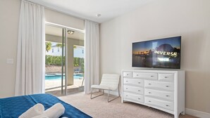 A hotel room with a bed, a TV, a white dresser, a chair, and a view of a swimming pool. - 10 bd Pool Home, spa, movie & game room (2302) (Kissimmee)