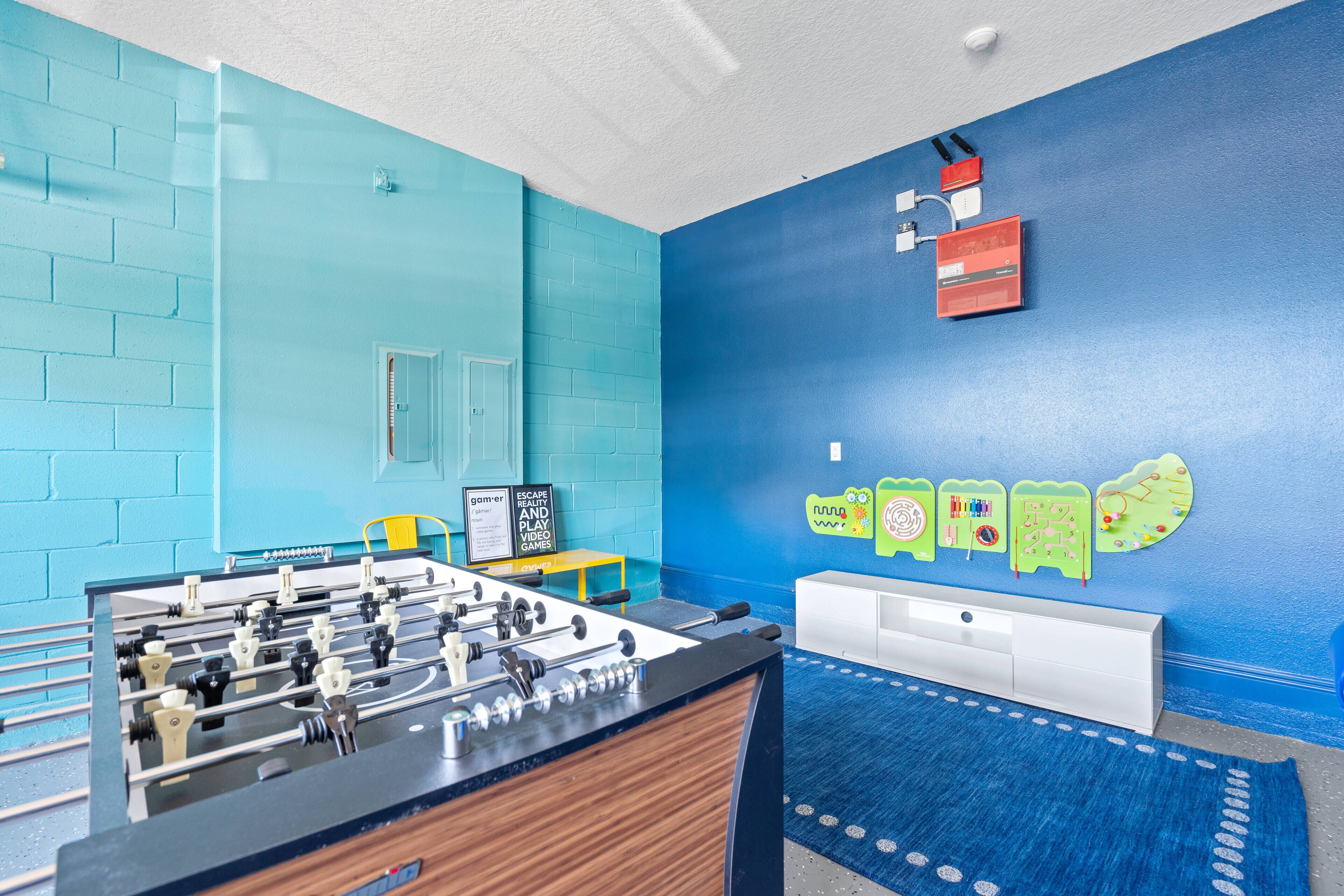 A room with a foosball table, a white cabinet, a blue wall, and a small table with a chair.
