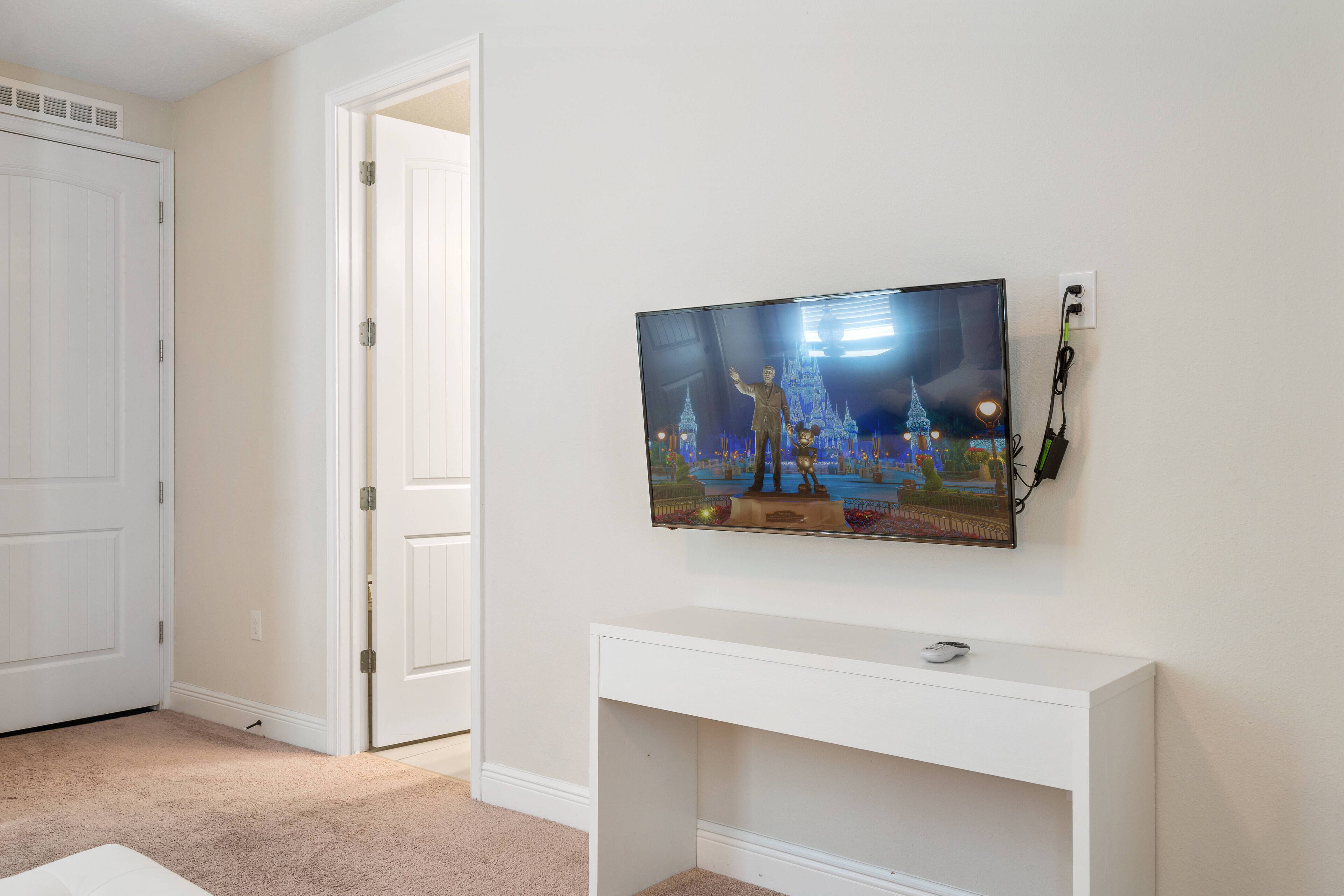 Una habitación con una consola blanca, un televisor de pantalla plana en la pared y una puerta cerrada.