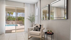 A modern living room with a beige armchair, a small side table with plants, and a large mirror on the wall. - 10 bd Pool Home, spa, movie & game room (2302) (Kissimmee)