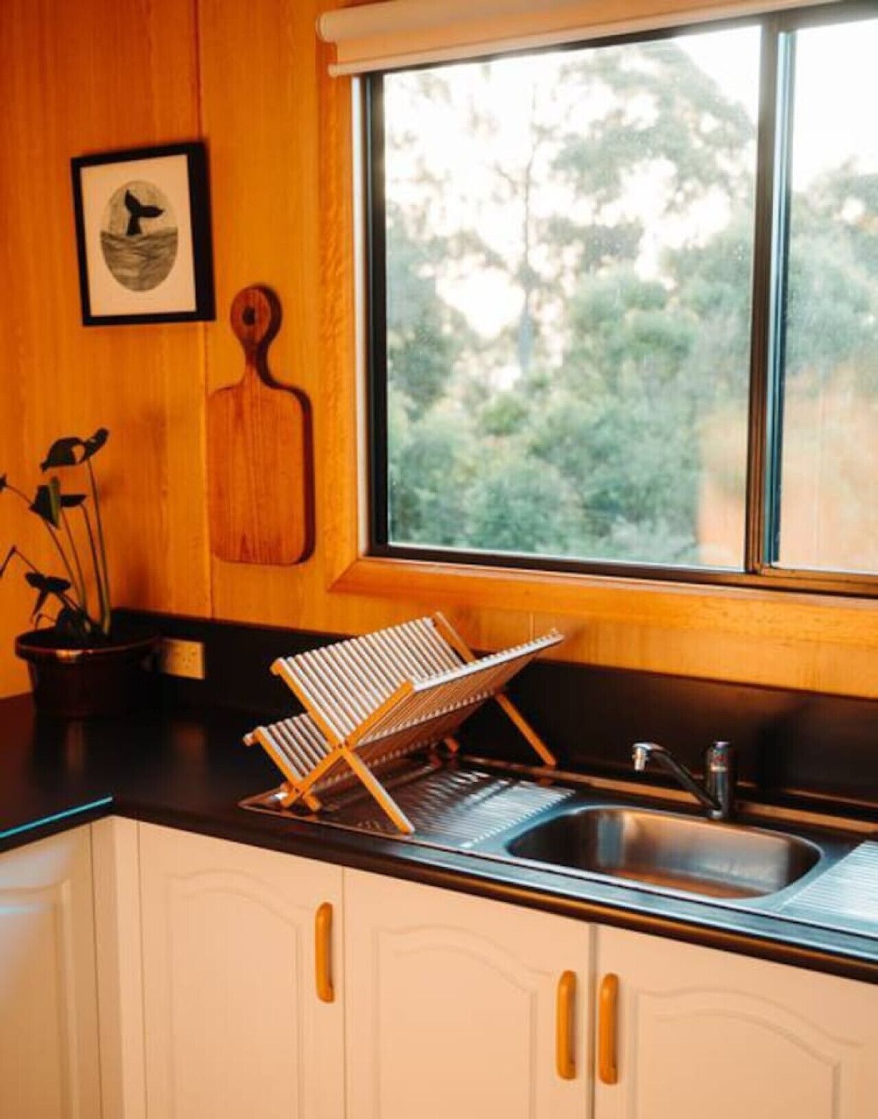 A kitchen with a wooden countertop, a hanging rack, a sink, and a window with a view of trees.
