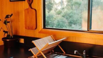 A kitchen with a wooden countertop, a hanging rack, a sink, and a window with a view of trees.