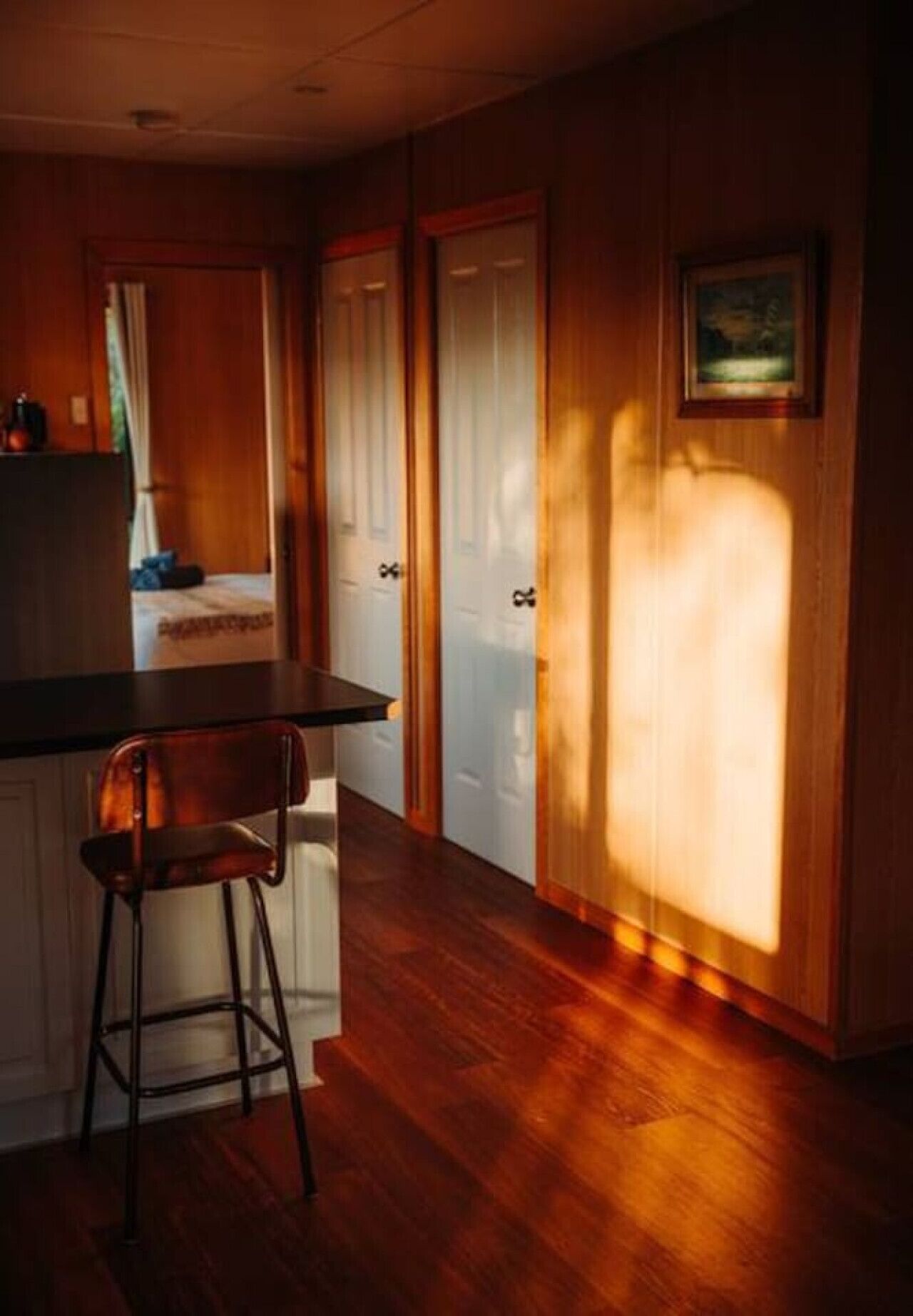 Una cocina con armarios de madera, un taburete de bar y una encimera. Hay dos puertas que conducen a otra habitación.